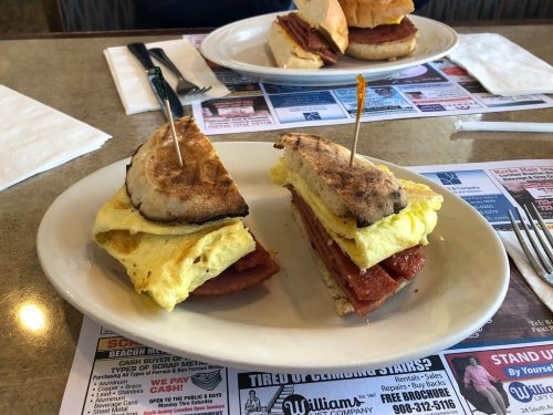 A plate with two sandwiches: one with an omelet and meat, the other with a bun and similar filling, on a diner table.