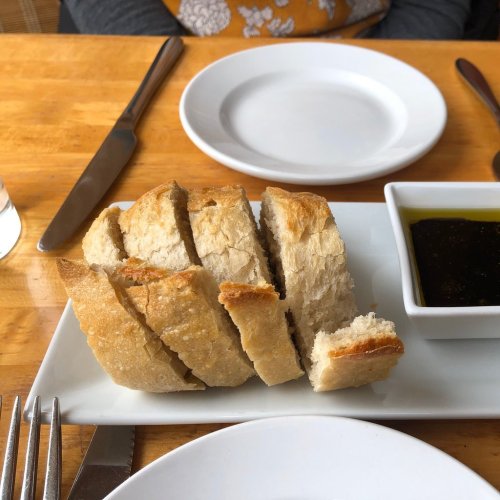A plate of sliced bread with a small dish of olive oil for dipping, set on a wooden table.