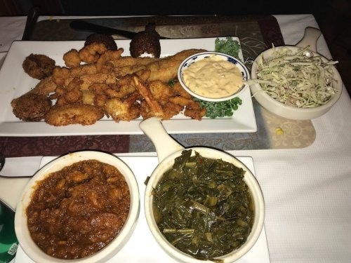 A platter of fried seafood, coleslaw, and two bowls of collard greens and chili on a table.