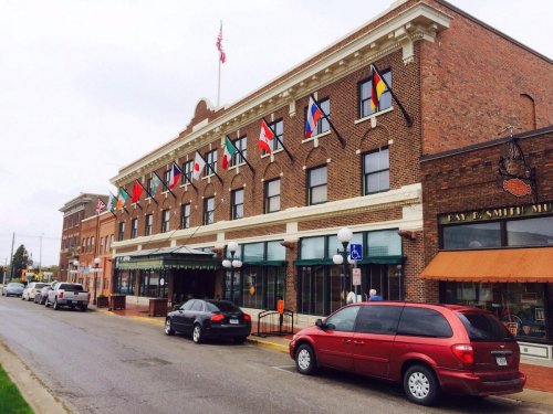 Historic brick building with flags from various countries hanging, parked cars in front, and a cloudy sky above.