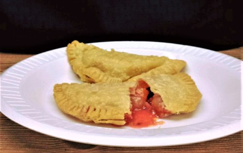 Two golden empanadas on a white plate, one partially open revealing a red filling.