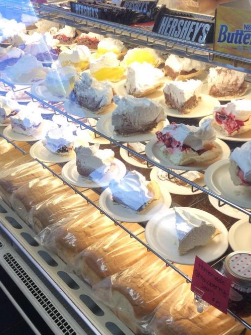 A display case filled with various slices of pie topped with whipped cream and a row of fresh bread loaves below.