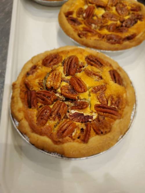 Two pecan pies with a golden crust and topped with whole pecans, displayed on a white tray.