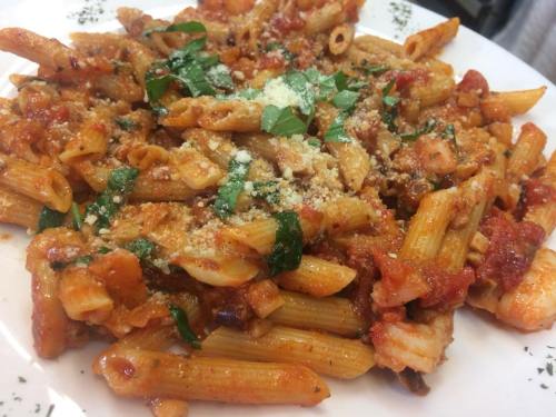 A plate of penne pasta topped with tomato sauce, herbs, and grated cheese, garnished with fresh basil.