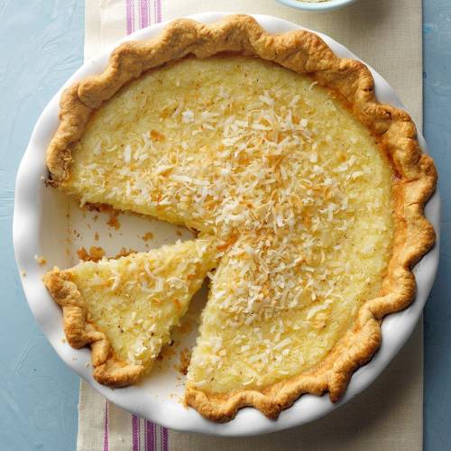 A coconut pie with a golden crust, topped with toasted coconut, with a slice cut out and placed beside it.