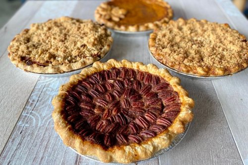 Four delicious pies on a wooden table: pecan, pumpkin, and two crumb-topped varieties.