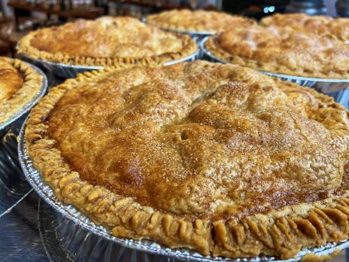 Close-up of freshly baked pies with golden, flaky crusts and a sprinkle of sugar on top, arranged in aluminum pie tins.