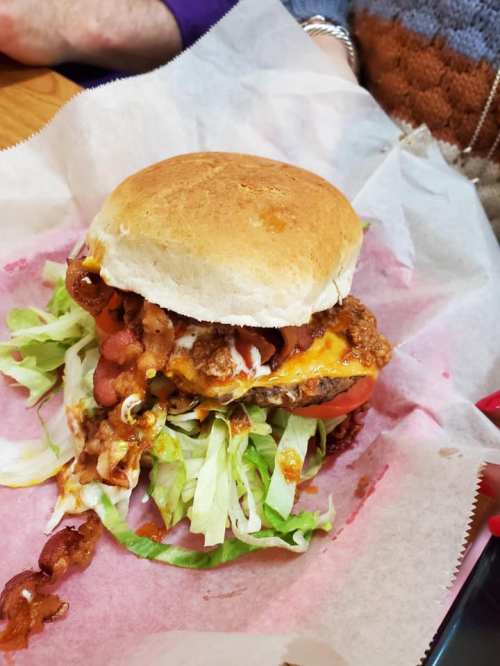 A hearty burger with lettuce, tomato, cheese, and bacon, served on a bun, resting on parchment paper.