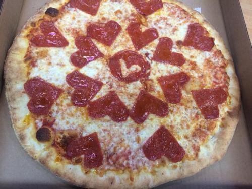 A heart-shaped pepperoni pizza with a circular pattern of heart-shaped pepperoni slices on a cheesy crust.
