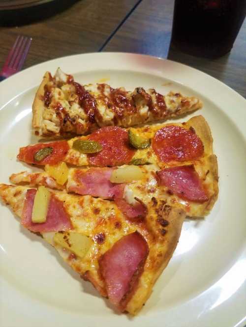 A plate with three slices of pizza: one with barbecue chicken, one with pepperoni and ham, and one with pineapple.