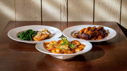 Three plates of food: grilled salmon with green beans, shrimp pasta, and a meat dish with crispy sides.