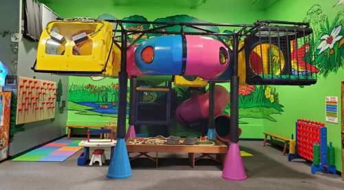 Colorful indoor play structure with slides, tunnels, and climbing areas against a vibrant mural backdrop.