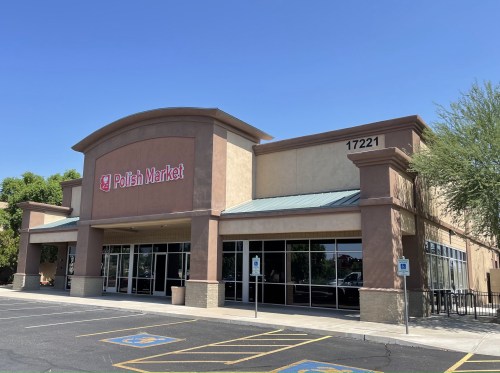 Exterior of Polish Market building with large windows and a sign, set in a parking lot under a clear blue sky.
