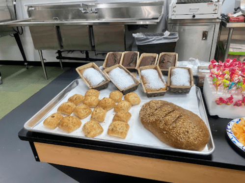 A tray of assorted baked goods, including small rolls, loaves of bread, and desserts, displayed in a kitchen setting.