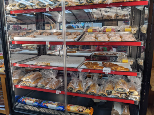 A display case filled with various baked goods, including pastries, rolls, and cookies, neatly arranged on shelves.