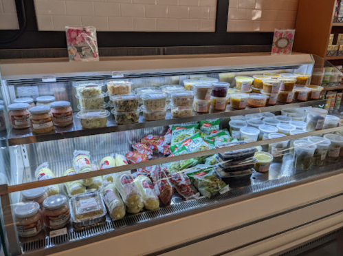 A refrigerated display case filled with various containers of salads, dips, and prepared foods.