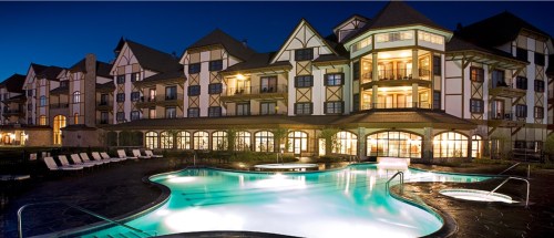 A beautifully lit hotel with a modern pool at dusk, featuring lounge chairs and elegant architecture.
