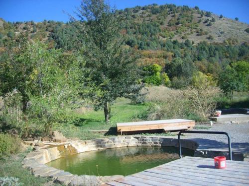 A serene outdoor scene featuring a stone pond, wooden deck, and lush green hills in the background under a clear blue sky.