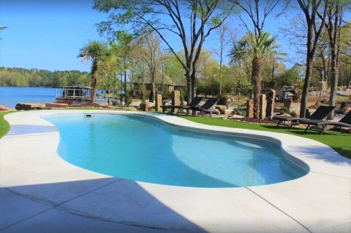 A serene pool surrounded by palm trees and lounge chairs, overlooking a calm lake and lush greenery.