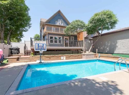 A backyard with a swimming pool, surrounded by trees and a two-story blue house with a deck.