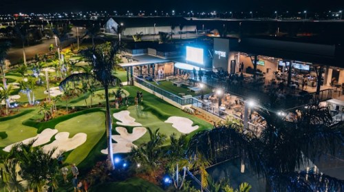 A vibrant night scene of a golf course with illuminated greens and a lively restaurant area in the background.