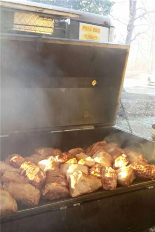 A barbecue grill filled with various meats, emitting smoke, under a sign that reads "Pork BBQ Turkey."