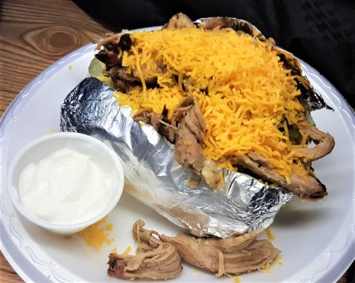 A foil-wrapped burrito topped with shredded cheese, served with a side of sour cream on a white plate.