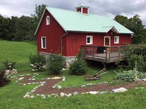 A red barn-style house with a green metal roof, surrounded by greenery and a stone pathway.