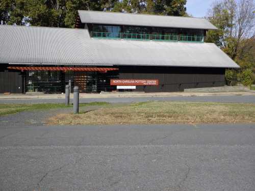 A modern building with a sloped roof, featuring large windows and a sign that reads "North Carolina Pottery Center."