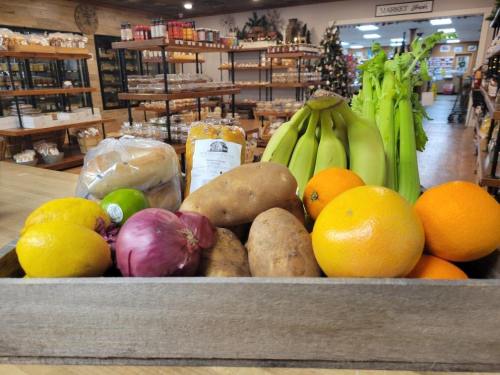 A wooden crate filled with fresh fruits and vegetables, including bananas, oranges, potatoes, and celery, in a market.