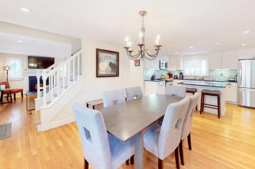 A modern dining area with a wooden table and gray chairs, leading to a bright kitchen with stainless steel appliances.