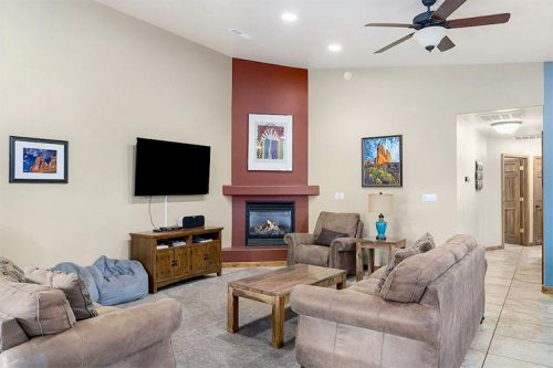 Cozy living room with a fireplace, comfortable seating, and artwork on the walls. A TV is mounted above a wooden console.