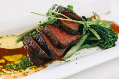 A beautifully plated dish featuring sliced beef, green vegetables, and a drizzle of sauce, garnished with microgreens.