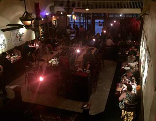 A bustling restaurant interior with diners at tables, a bar area, and warm lighting creating a cozy atmosphere.