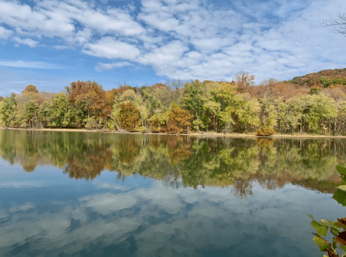 A serene lake reflecting colorful autumn trees under a partly cloudy sky.