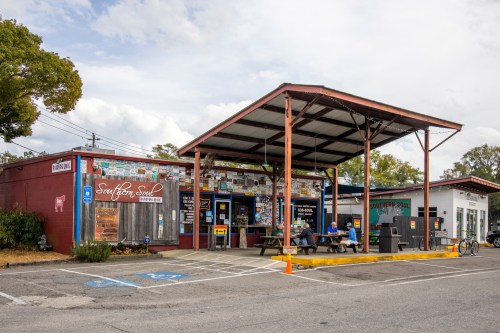 A colorful building with a covered patio, featuring signs and artwork, houses Southern Soul BBQ and Southern Pool.
