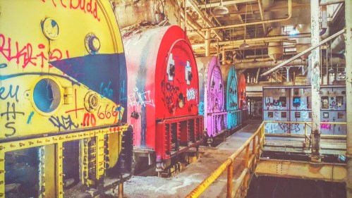 Abandoned industrial space with colorful, graffiti-covered machinery and rusted structures.