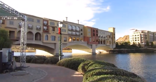 A scenic view of colorful buildings along a waterfront, with a bridge and lush greenery in the foreground.