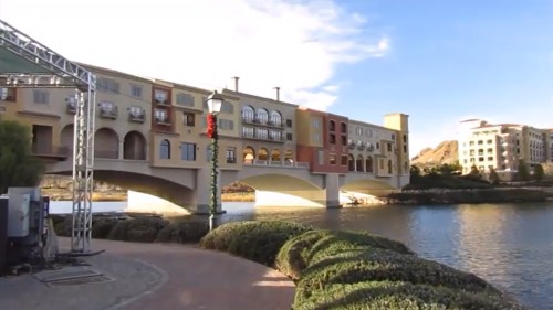Scenic view of colorful buildings along a waterfront with a bridge and landscaped greenery under a clear blue sky.