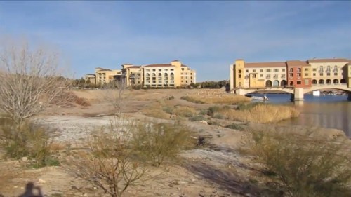 A view of a riverbank with buildings in the background and sparse vegetation along the shore.