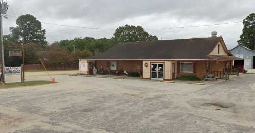 A brick building with a sloped roof, labeled "Meadow Restaurant," surrounded by a gravel parking lot and trees.