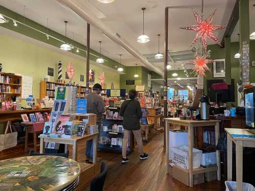 A cozy bookstore interior with wooden shelves, colorful books, and decorative star lights. Two people browse the shelves.