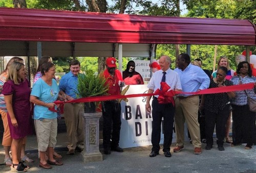 A group of people gathers to cut a red ribbon at a new restaurant opening, celebrating with smiles and balloons.