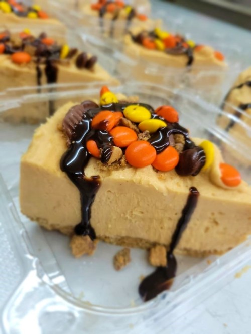 A slice of creamy peanut butter cheesecake topped with chocolate drizzle and colorful candy pieces.