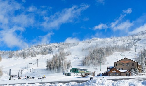 A snowy mountain landscape with a ski resort building and ski lifts under a bright blue sky.