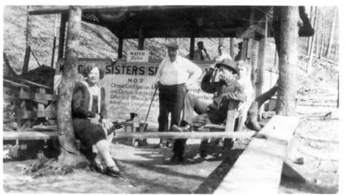 A black and white photo of five people at a rustic outdoor setting, with a sign for "Sisters Spring" in the background.