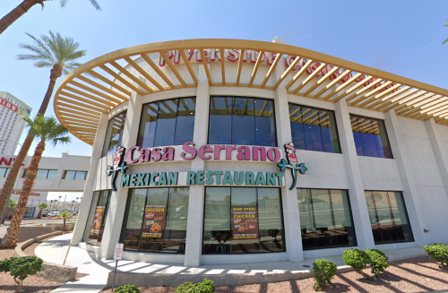 Exterior of Casa Serrano Mexican Restaurant, featuring a modern design and large windows, surrounded by palm trees.