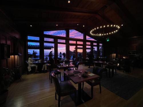Cozy restaurant interior with elegant tables, large windows showcasing a colorful sunset, and guests enjoying the view.