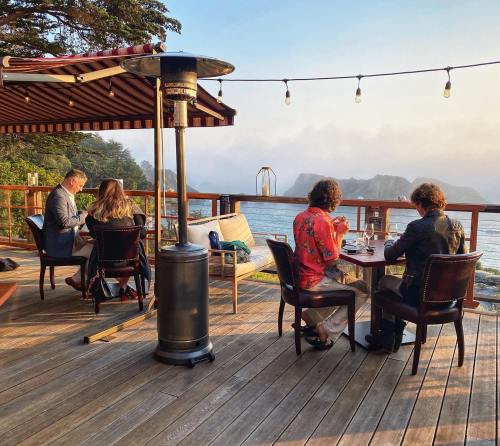A scenic outdoor dining area with people enjoying a meal, overlooking a misty ocean view at sunset.