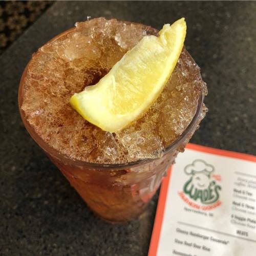 A refreshing drink with ice and a lemon slice, placed on a table next to a menu.
